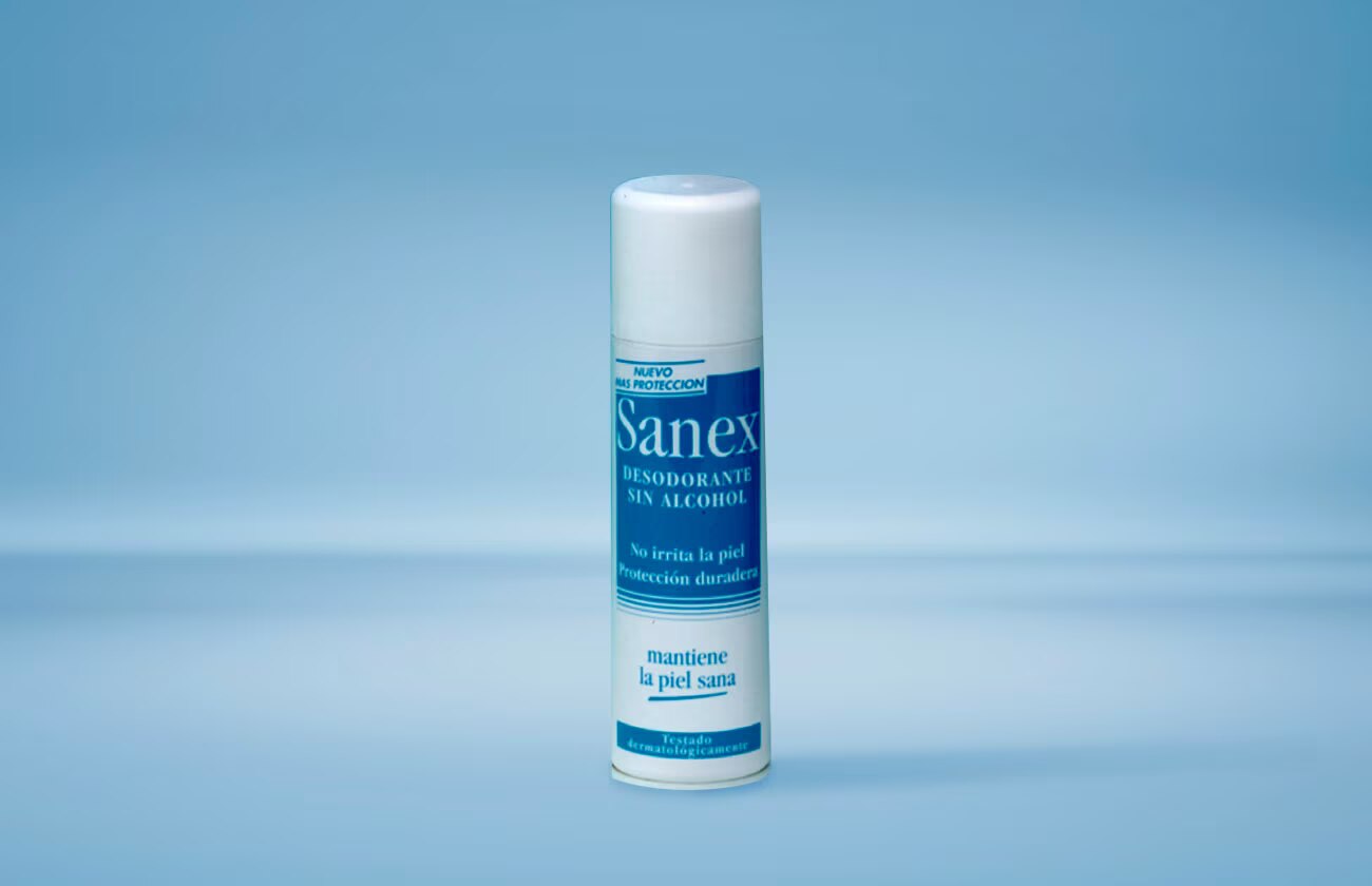 Een spuitbus Sanex deodorant zonder alcohol, met een witte dop, tegen een lichtblauwe achtergrond.