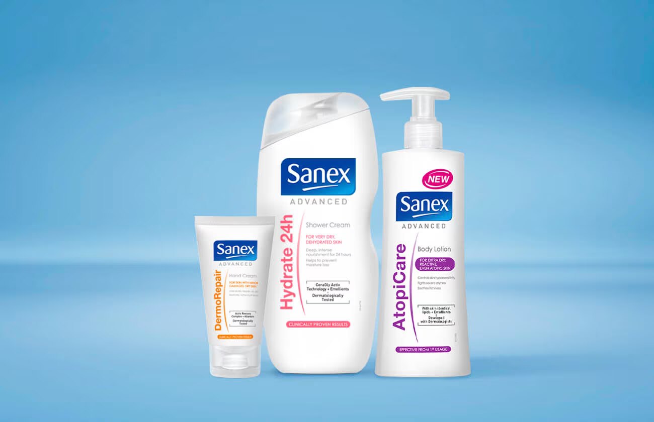 Drie producten uit de 'Sanex Advanced' lijn: een tube DermoRepair handcrème, een fles Hydrate 24h douchecrème en een pompflacon AtopiCare bodylotion.